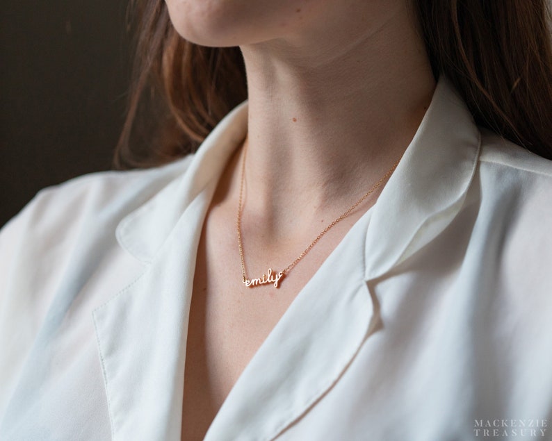 May include: A gold chain necklace with the name "emily" spelled out in cursive script.