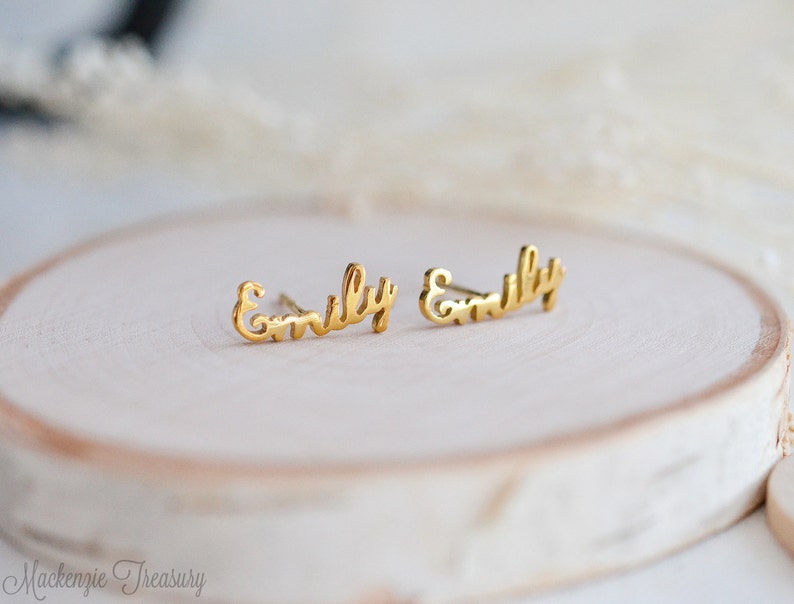 May include: A pair of gold-toned earrings with the name "Emily" written in cursive script.