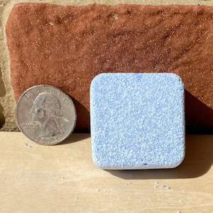 May include: A single, light blue dishwasher tablet, about the size of a quarter, with a grainy texture.