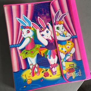 May include: A pink Lisa Frank binder with a design of three cartoon bunnies in ballet costumes on a stage with pink curtains. The bunnies wear tutus and flower crowns. The binder has the text "THE FANTASTIC WORLD Lisa Frank".