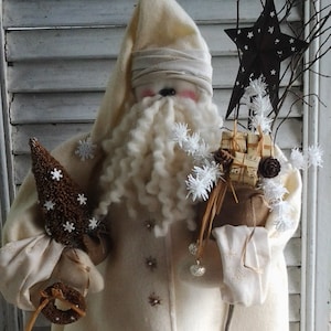 May include: A white felt Santa Claus doll with a white beard and a white hat. The doll is holding a brown twig with a star and a small brown tree. The doll is standing on a wooden stump with white snow.