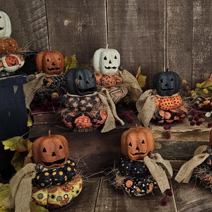 May include: A collection of eight handmade Halloween jack-o'-lantern decorations. Each jack-o'-lantern is made of fabric and has a different pattern. The jack-o'-lanterns are arranged on a wooden surface with fall foliage.