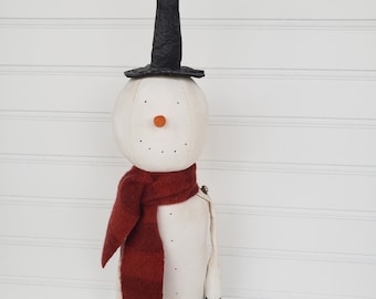 May include: A white snowman with a black pointed hat and a red scarf. The snowman is holding a small green plant in a white pot.