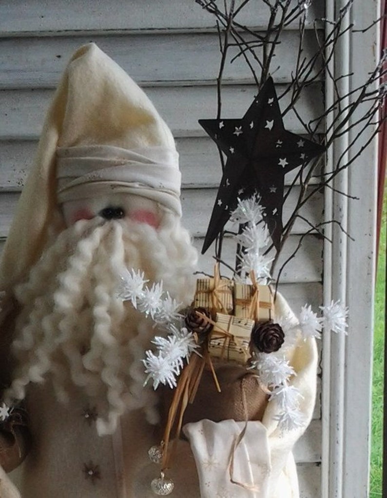May include: A white fabric Santa Claus doll with a long white beard and a white hat. The doll is holding a burlap sack filled with small wrapped gifts and a white star on a twig.
