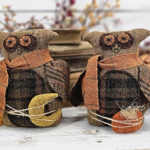 May include: Two brown felt owls with orange scarves and black eyes. One owl is holding a yellow crescent moon and the other is holding a small orange pumpkin.