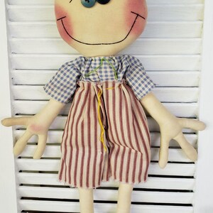 May include: A handmade rag doll with brown hair, a blue and white checkered shirt, red and white striped pants, and black shoes. The doll has a smiling face with rosy cheeks and blue eyes.