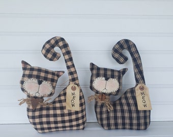 May include: Two black and tan plaid fabric cat figurines with brown eyes and a stitched nose. Each cat has a brown fabric tag that says "MEOW" hanging from its tail.