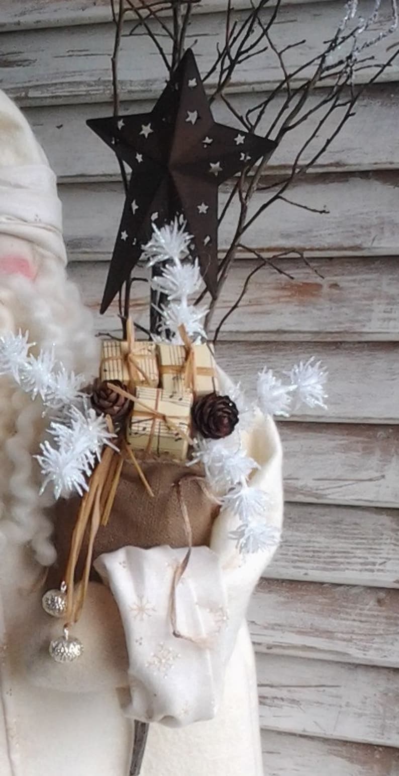 May include: A white, fuzzy, snowman-like figure with a brown sack filled with wrapped gifts and a rustic star on top. The figure is decorated with white, fluffy, snowflake-like embellishments and brown twigs.