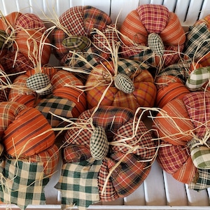 May include: A collection of nine handmade patchwork pumpkins in shades of orange, brown, and green. The pumpkins are made from plaid fabric and have a rustic, farmhouse style.