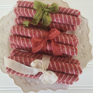 May include: Three sets of red and white striped fabric dish towels tied with different colored ribbons. The towels are folded and stacked on a white plate.