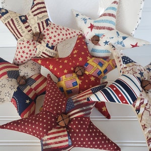 May include: Six handmade patriotic star-shaped pillows with red, white, and blue fabric. The pillows are decorated with stars, stripes, and the words "God Bless America".