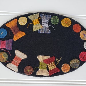 May include: A black felt oval rug with a colorful design of spools of thread and buttons. The rug is perfect for a sewing room or craft area.