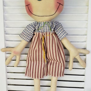 May include: A handmade rag doll with a blue and white checkered shirt, red and white striped pants, and black shoes. The doll has a smiling face with rosy cheeks and blue eyes.
