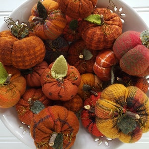 May include: A bowl filled with handmade felt pumpkins in various shades of orange, brown, and red. The pumpkins have a rustic, autumnal feel and are perfect for fall decor.