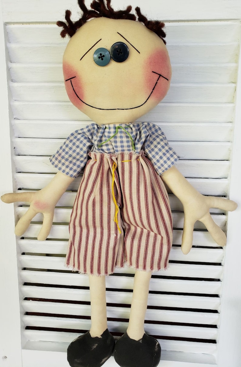 May include: A handmade rag doll with brown yarn hair, blue eyes, and a red and white striped outfit. The doll is smiling and has rosy cheeks.