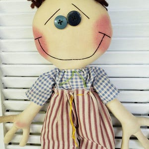 May include: A handmade rag doll with brown yarn hair, a smiling face with blue button eyes, a blue and white plaid shirt, and red and white striped pants.
