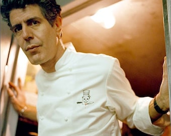 Peut inclure: Un homme portant une veste de chef blanche avec un petit logo de chef sur la poche gauche de la poitrine. Le logo est un chef de dessin animé avec un couteau et un chapeau de chef.