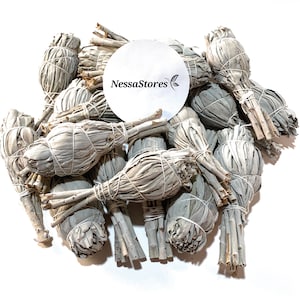 May include: A pile of white sage smudge sticks, tied with twine, ready for burning. The sticks are bundled together in a loose, organic arrangement. A white circle label with the text "NessaStores" is visible in the image.