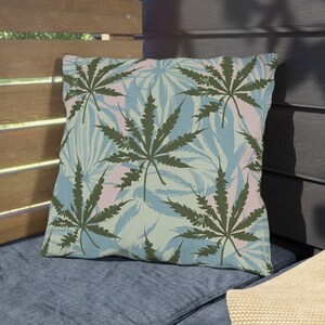 Puede incluir: Una almohada decorativa con un patrón de hojas azules y verdes. La almohada presenta un patrón repetitivo de grandes hojas verdes sobre un fondo azul claro con toques de rosa.