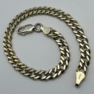 May include: A silver-toned metal chain bracelet featuring interlocking flat links. The bracelet includes a lobster claw clasp mechanism at one end and a small metal tag stamped with the word ITALY at the other end, forming a circular shape.