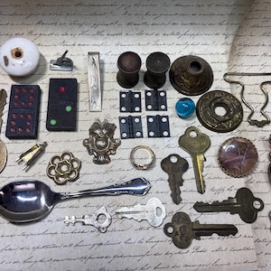 May include: A collection of vintage hardware and decorative items, including keys, dominoes, hinges, and a spoon. The items are in various metallic finishes and colors, arranged on a paper background with handwritten script.