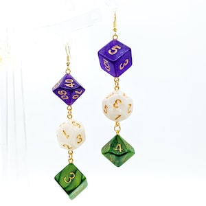May include: Purple, white, and green dice dangle from gold chains, forming a pair of earrings. Each die has gold numbers.