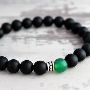 Puede incluir: Un brazalete de cuentas negras con una piedra preciosa verde y una cuenta de acento plateada.