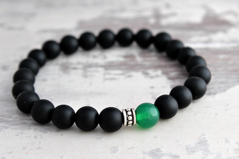 Puede incluir: Un brazalete de cuentas negras con una piedra preciosa verde y una cuenta de acento plateada.