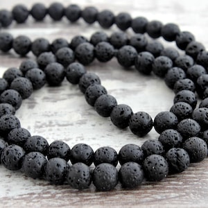 May include: A strand of black lava rock beads. The beads are round and have a rough, textured surface.