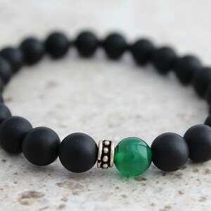 Puede incluir: Pulsera de cuentas mate negras con una sola cuenta de piedra preciosa verde y una cuenta espaciadora plateada.