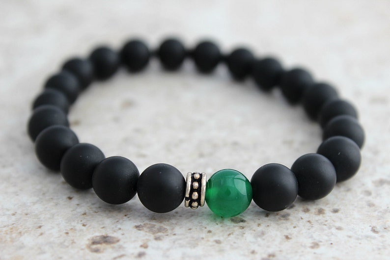 Puede incluir: Pulsera de cuentas mate negras con una sola cuenta de piedra preciosa verde y una cuenta espaciadora plateada.