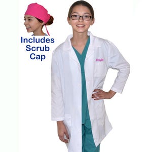 May include: A white lab coat with the name "Kayla" embroidered in pink. The image includes a teal scrub top and pants, and a pink scrub cap. The text "Includes Scrub Cap" is also visible.