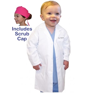 May include: A child wearing a white lab coat over a blue scrub top and pants. The lab coat has a button closure and a pocket. The text "Your Name" is embroidered on the chest. Includes a pink scrub cap.