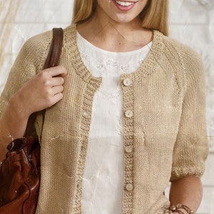 May include: A tan, short-sleeved cardigan with a round neckline and button closure. The knitted sweater is worn over a white blouse. A brown leather purse is visible, along with a beaded bracelet.