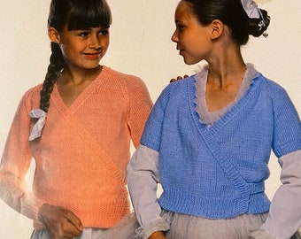 May include: Two young girls wearing ballet tutus and knitted sweaters. The girl on the left is wearing a peach sweater and the girl on the right is wearing a light blue sweater.
