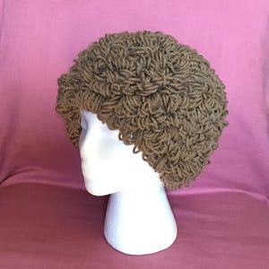 Może przedstawiać: Brązowy, dziergany na drutach kapelusz o kręconym, fakturowanym wzorze. Kapelusz jest prezentowany na białej głowie manekina.