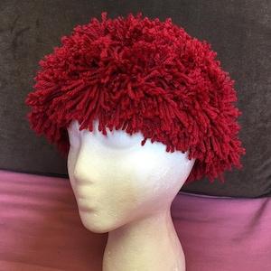 May include: A red fuzzy hat made from yarn. The hat is on a white styrofoam head.