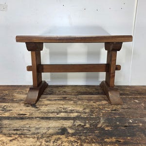 May include: A rustic, wooden bench with a rectangular top and sturdy, angled legs. The bench is constructed from dark-stained wood, showcasing the natural grain. The design features a horizontal support beam connecting the legs, adding to its stability and vintage aesthetic.