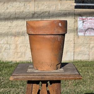 May include: A weathered terracotta plant pot with a wide, thick rim and a tapered body. The surface displays a natural, earthy orange-brown color with visible signs of wear, including minor surface chips, soil residue, and subtle texture variations.