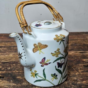 May include: White porcelain teapot with a floral and butterfly design. The teapot has a bamboo handle and a gold lid.