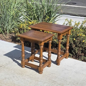 May include: Two rectangular wooden side tables with a medium brown finish. Each table features a flat top surface and four legs with decorative turned detailing, connected by horizontal support bars near the base of the furniture.