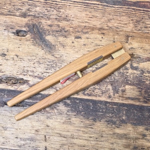 May include: A wooden nutcracker with brass details and a brush. The nutcracker is made of light-coloured wood and has a classic design. It is lying on a weathered wooden surface.