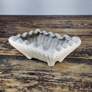 Op de afbeelding: Een vintage, crèmekleurige keramische plantenbak met een gespikkelde afwerking. De rechthoekige plantenbak heeft een geschulpte rand en wordt ondersteund door drie kleine voetjes. De buitenkant heeft verticale, geribbelde details. Een decoratief item voor planten.