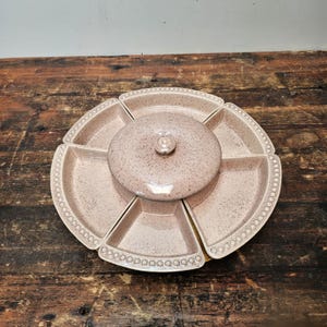 May include: A pink ceramic serving dish with a lid and six individual sections. The dish has a speckled finish and a beaded edge.