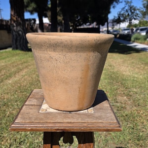 May include: A tapered terracotta plant pot with a matte finish, featuring a light tan color with subtle dark speckling and a weathered appearance. The pot has a wide, rounded rim and a smooth, unglazed surface texture throughout.