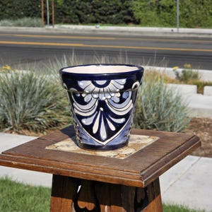 Könnte beinhalten: Ein blau-weißer Keramik-Blumentopf mit einem dekorativen Blumendesign. Der Topf steht auf einem Holztisch mit einem Fliesen-Einsatz. Der Topf ist etwa 20 cm hoch.