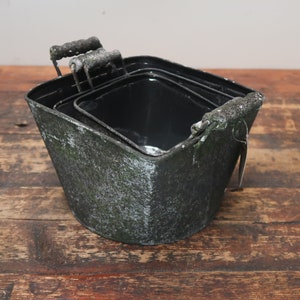 May include: Set of three black metal planters with distressed green paint and wooden handles. The planters are nested inside each other.