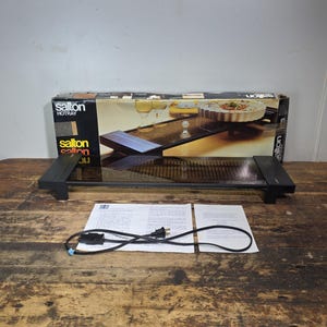 Puede incluir: Una bandeja calentadora Salton Hotray rectangular con superficie de cristal marrón oscuro y asas laterales negras. El artículo incluye su embalaje original de cartón con imágenes, un cable de alimentación negro y dos manuales.