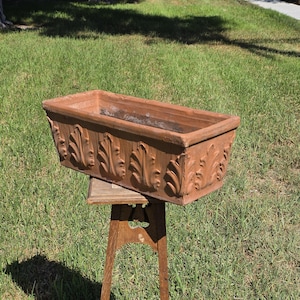 May include: A rectangular terracotta planter featuring a repeating embossed leaf pattern along the exterior sides. The planter has a wide, open top and a flat base, showcasing a natural reddish-brown clay finish with visible texture.
