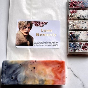 Puede incluir: Un derretimiento de cera con un personaje de la serie de videojuegos Resident Evil, Leon Kennedy. El derretimiento de cera es de color azul claro, blanco y naranja con motas negras. El derretimiento de cera est&aacute; empaquetado en una bolsa de papel blanca con una etiqueta que dice "Resident Evil" y "Leon Kennedy". La etiqueta tambi&eacute;n incluye las notas de aroma: cuero, cedro, teca, hoja de tabaco, s&aacute;ndalo, pachul&iacute;, vainilla, &aacute;mbar, caoba. El derretimiento de cera es de 3 oz netos / 85 ml y se verti&oacute; en Smyrna, GA.